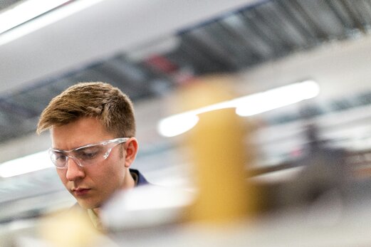 Junger Mann mit Schutzbrille in einer Fertigung.
